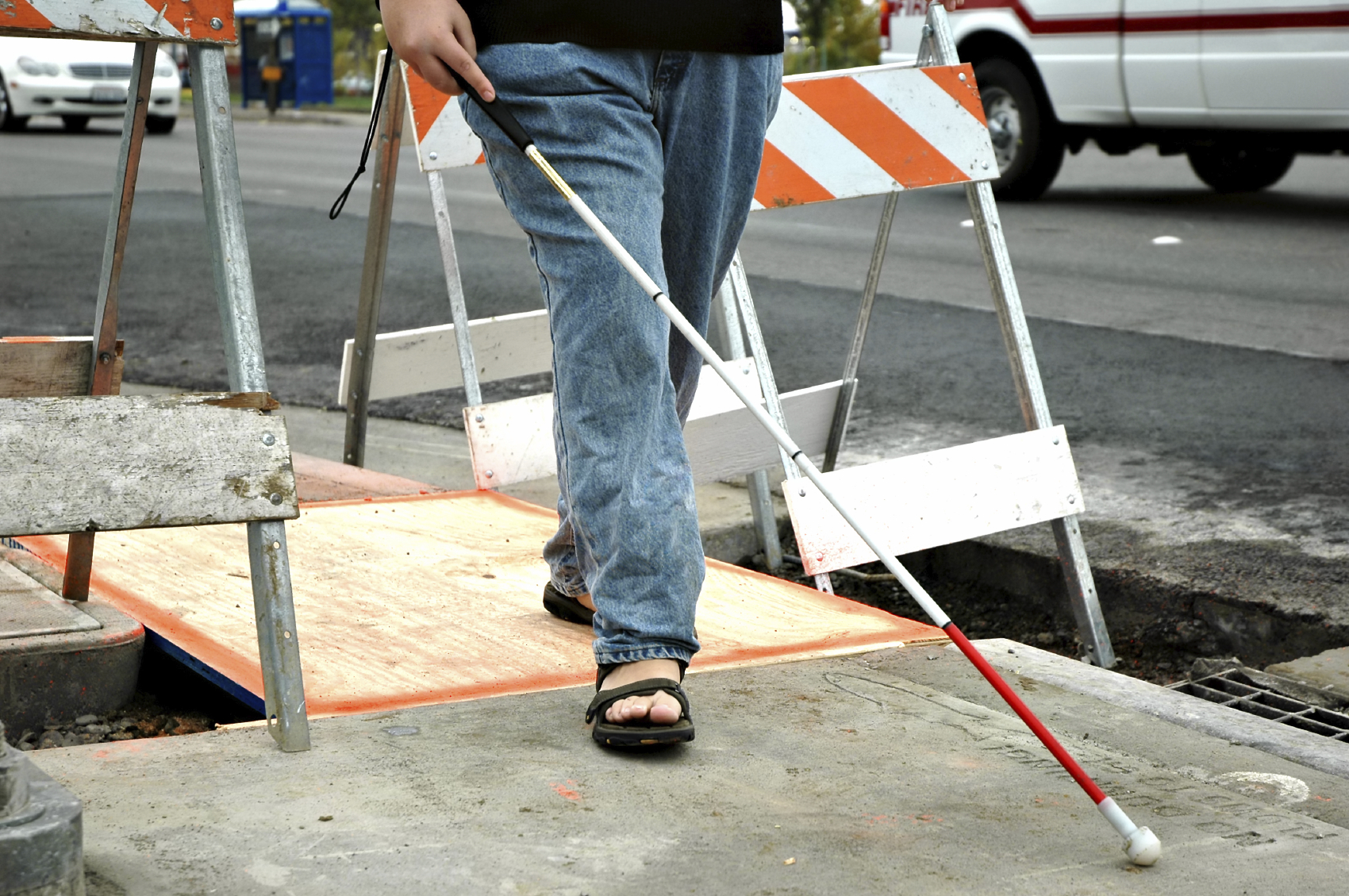 person walking across construction zone using a white cane with red end